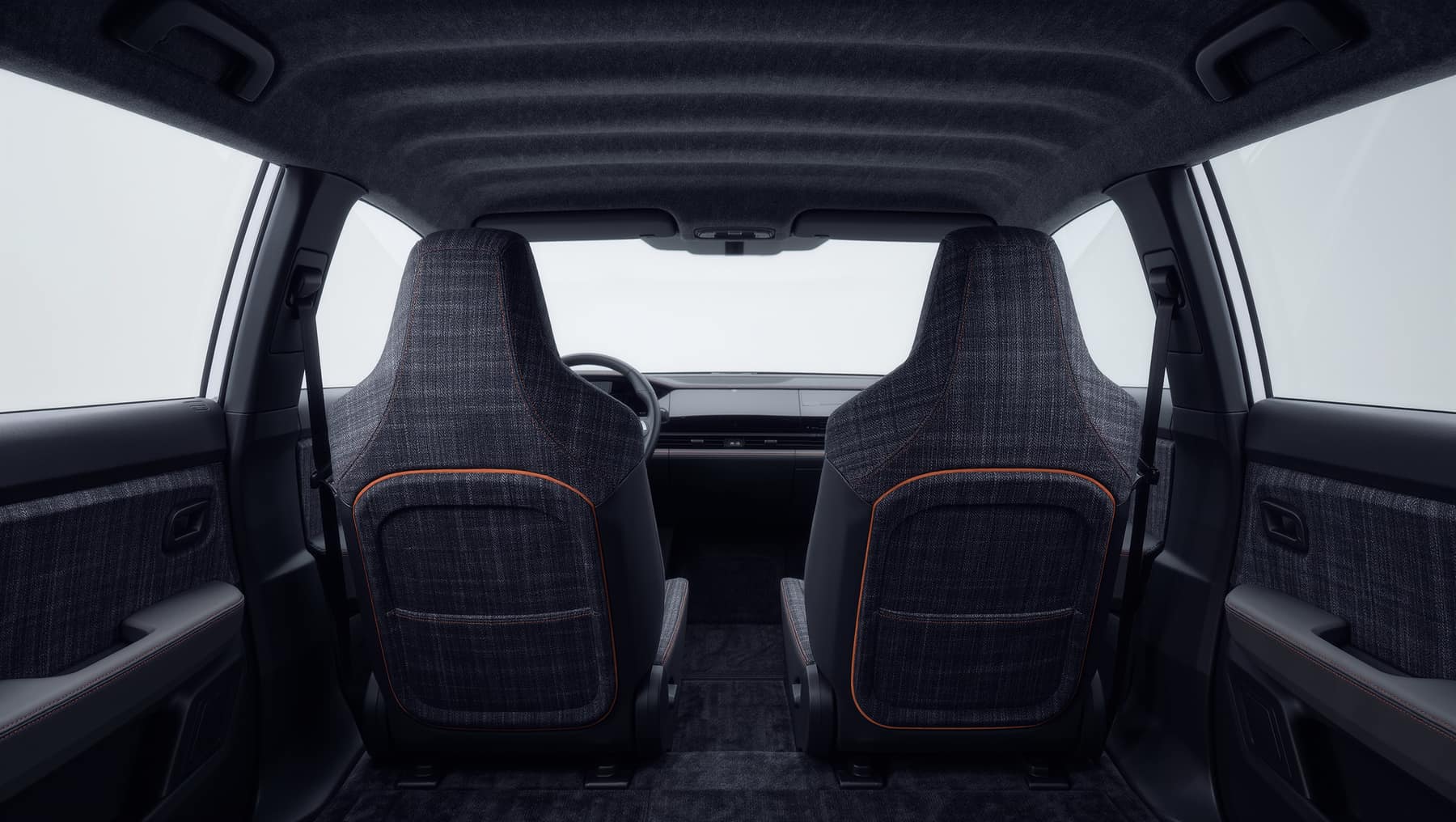 The interior of a contemporary vehicle seen from the rear seat: charcoal woven seat facings with orange contrast stitching, a felted headliner and textile-wrapped door cards.