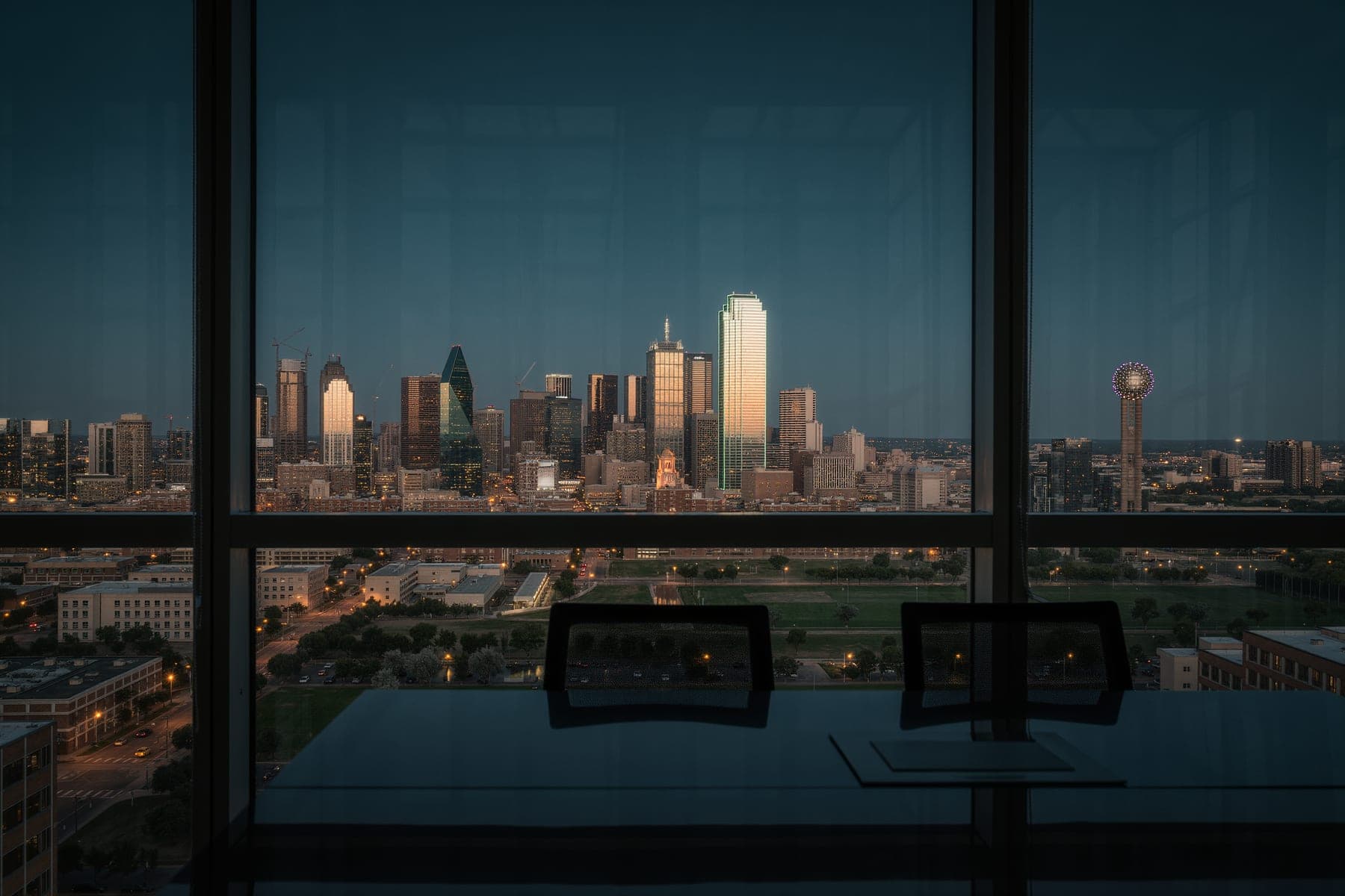 A Texas downtown skyline at blue hour seen through the floor-to-ceiling glass of a high-rise office.