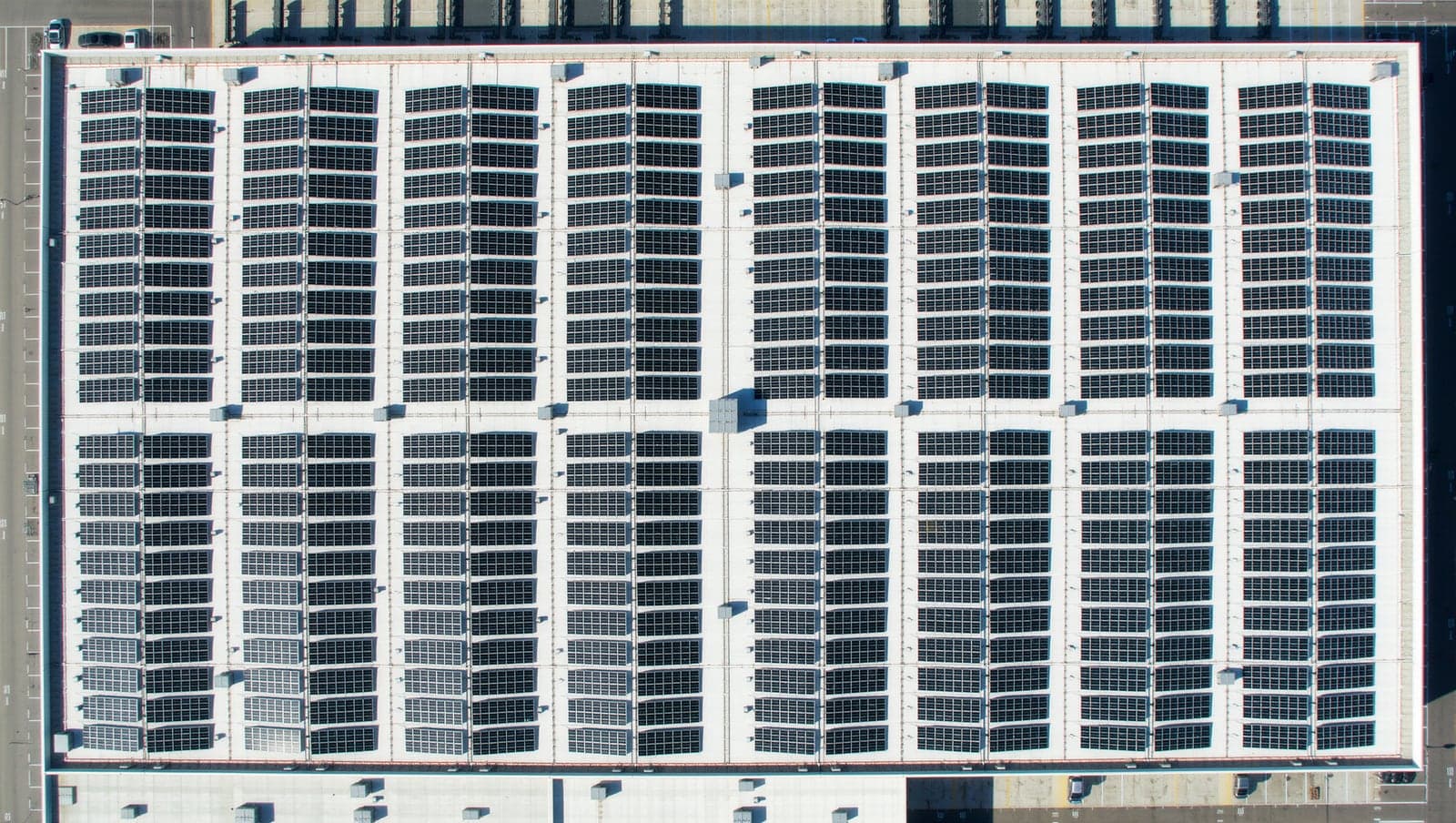 Straight-down aerial view of a commercial flat-roof solar array, uniform panel rows separated by clean walkways.