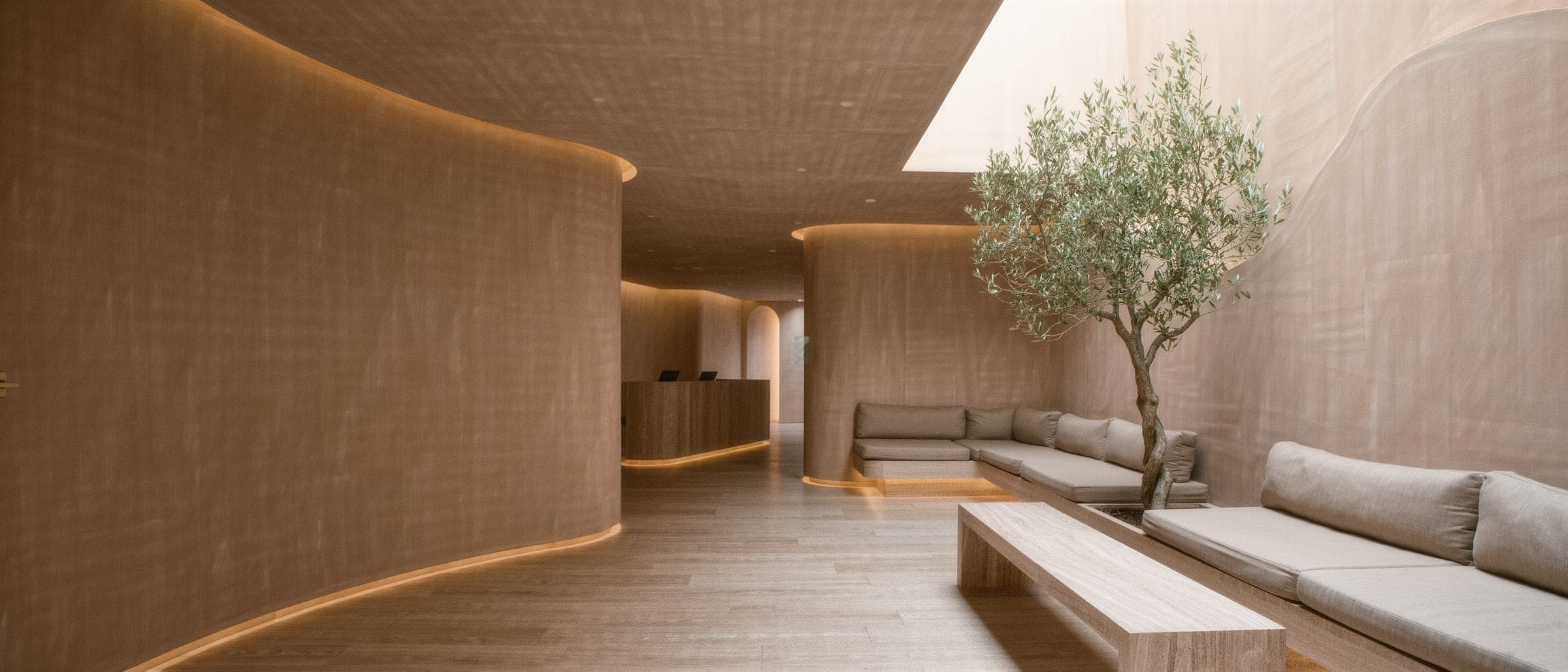 The reception lounge of a modern medical spa: warm plaster walls, curved archways, travertine seating and soft daylight.