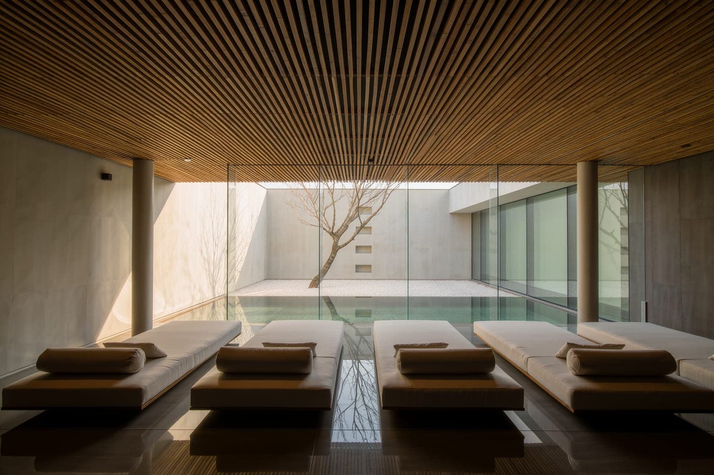 A relaxation lounge with low linen daybeds facing a glass wall onto a gravel courtyard.