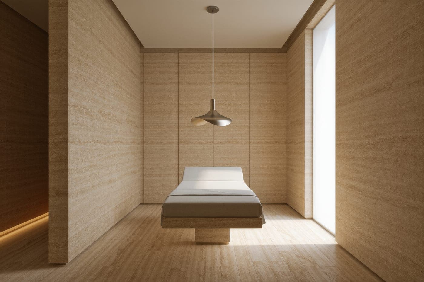 A treatment suite with honed travertine walls, a floating linen-covered bed and a single blade of daylight across the floor.