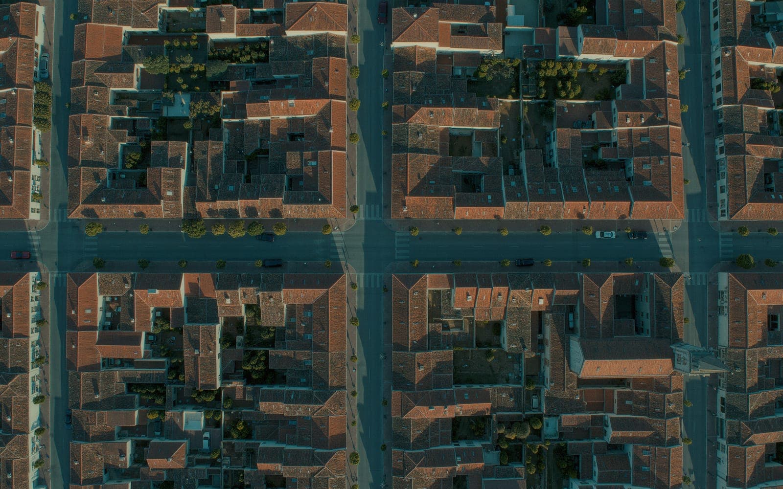 A small American town seen from directly above at golden hour, a tidy street grid with terracotta rooftops and a tree-lined main street