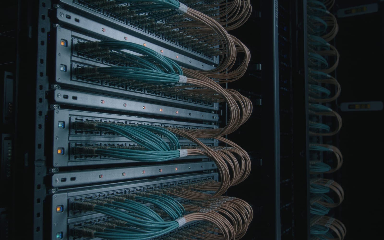 A tidy server rack at an angle in a dim room with neat rows of teal and amber network cables and small glowing indicator lights