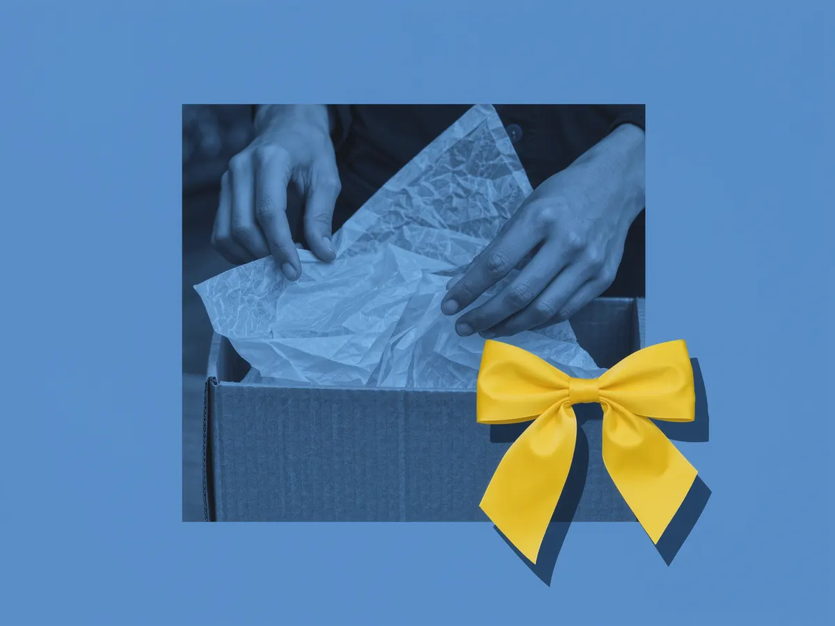 Hands packing a cardboard shipping box with tissue paper and a yellow bow.