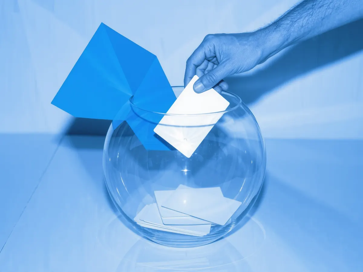 Hands dropping a blank card into a glass fishbowl full of cards.