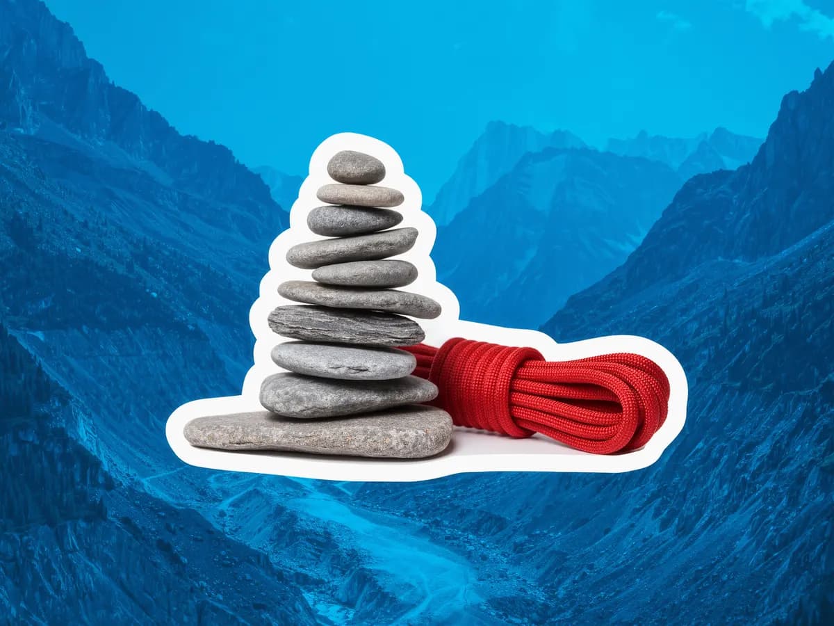 A cairn of balanced flat stones beside a coil of red climbing rope, over a blue photograph of a mountain trail.