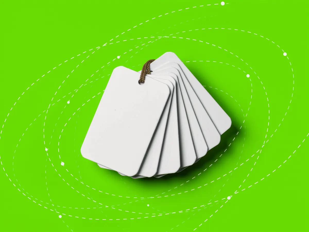A bundle of blank paper luggage tags on strings against a bright green background.