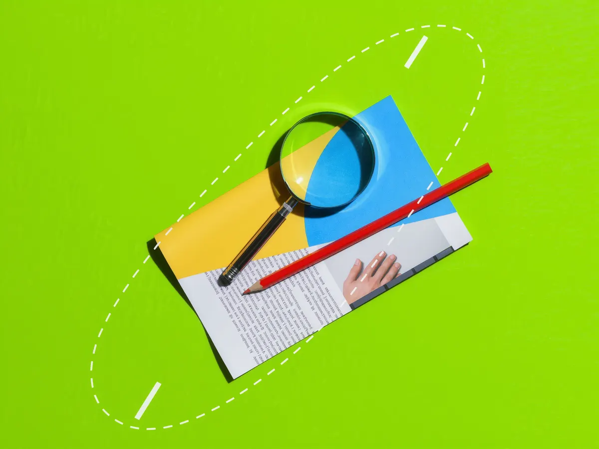A magnifying glass and a red pencil resting on a printed web page against a bright green background.
