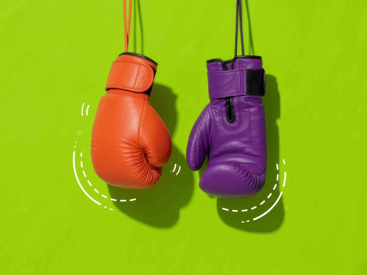 Two boxing gloves, one orange and one purple, hanging side by side on a lime green background.