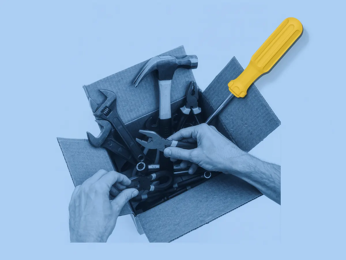 Hands sorting hand tools in a cardboard box, with a yellow screwdriver popping out of the photo.