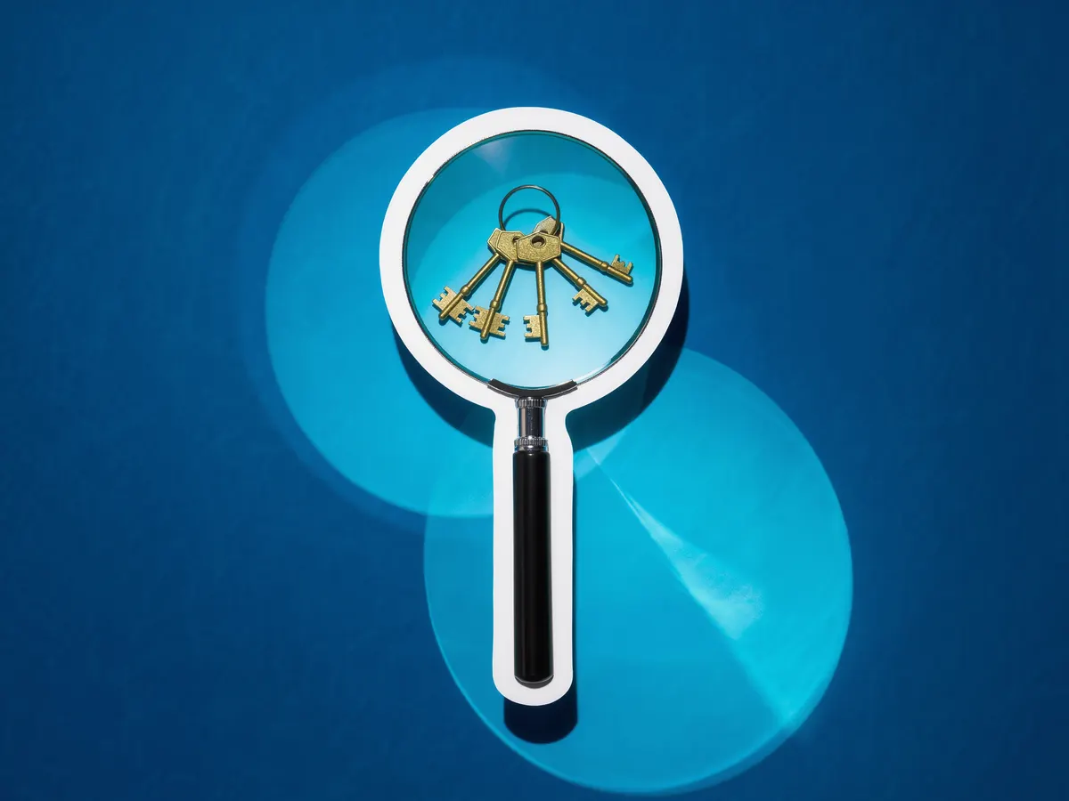 A jeweler's loupe magnifying a small pile of brass keys against a blue duotone background.
